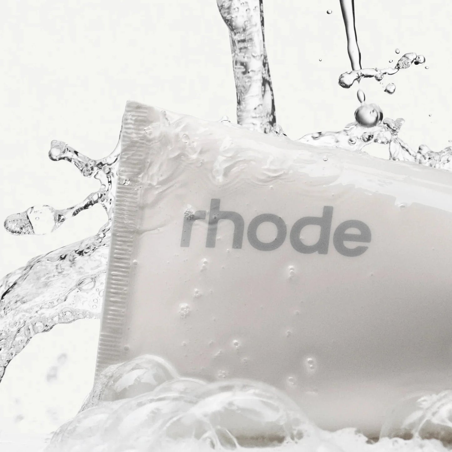 White bar of soap with 'rhode' branding surrounded by water droplets on a white background
