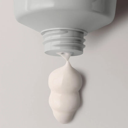 Close-up of a white tube with cream being squeezed out on a light gray background