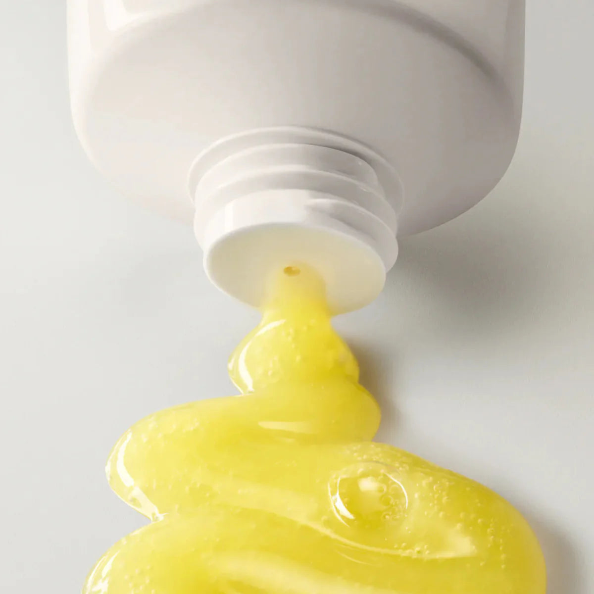 Close-up of a white tube with yellow cream being squeezed out on a light gray background