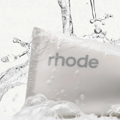White bar of soap with 'rhode' branding surrounded by water droplets on a white background