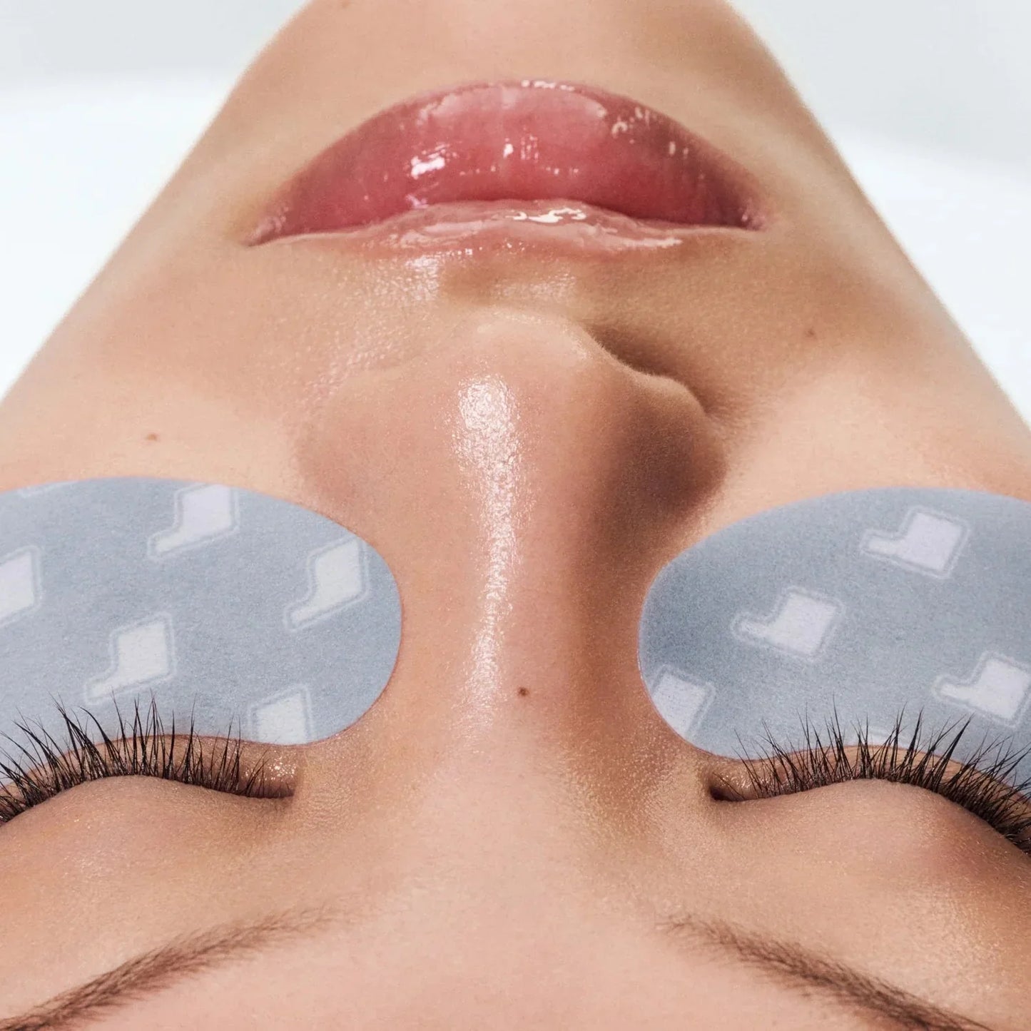 Close-up of a person's face with eye patches on a neutral background