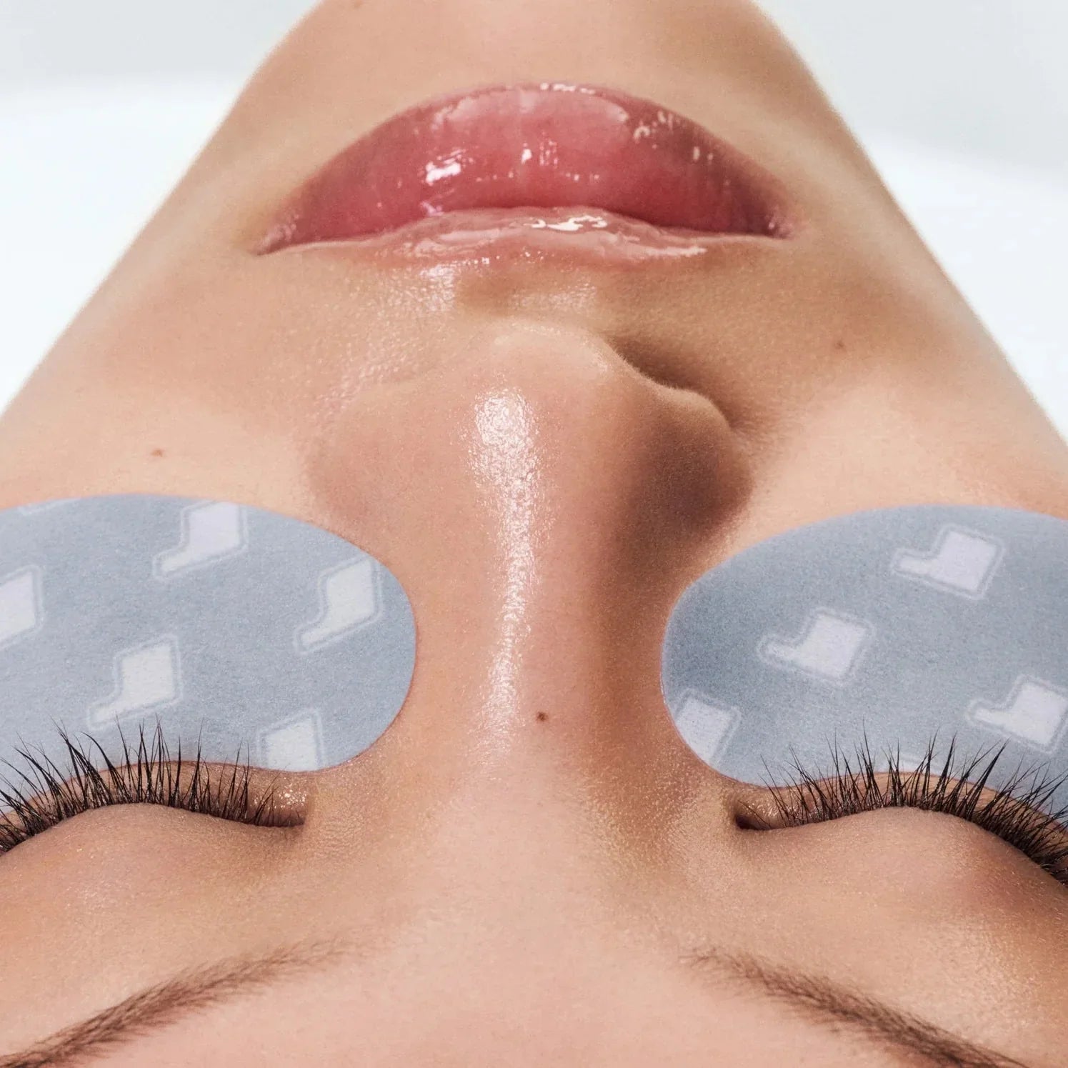 Close-up of a person's face with eye patches on a neutral background