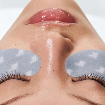 Close-up of a person's face with eye patches on a neutral background